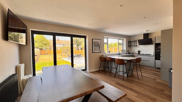 A modern kitchen with a central island, bar stools, and a dining table.