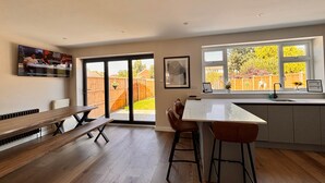A modern kitchen with a dining area, large windows, and a TV mounted on the wall.