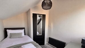 A bedroom with a bed, a radiator, a desk, and a door with a mirror.