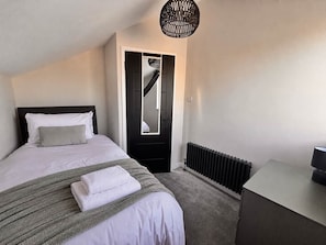 A bedroom with a bed, a radiator, a desk, and a door with a mirror.