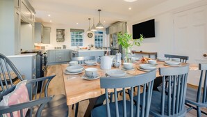 A modern kitchen with a central island, dining table with chairs, and a large window. - 4 Bed in Trethevy (oc-s33745) (Bossiney)