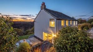 A white house with a tiled roof, a chimney, and a garage door. - 4 Bed in Trethevy (oc-s33745) (Bossiney)