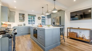 A modern kitchen with grey cabinets, a central island, stainless steel appliances, pendant lighting, and a large window. - 4 Bed in Trethevy (oc-s33745) (Bossiney)