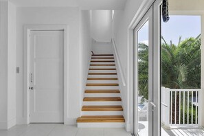 A staircase with wooden steps leading to a landing, a white door, and a view of palm trees through a glass door. - Gulfside Oasis a Dream on the Gulf (Marathon)