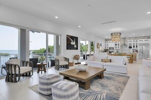 A spacious living area with a large window overlooking a body of water, a dining area with a chandelier, and a kitchen with white cabinetry. - Gulfside Oasis a Dream on the Gulf (Marathon)