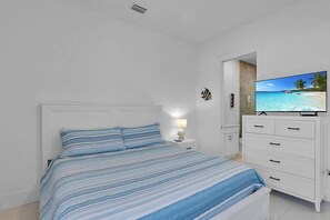 Un dormitori amb un llit, una televisió damunt d'una commode i una porta que dona a una altra habitació.