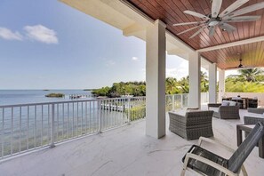 A covered outdoor area with a view of the sea, featuring a ceiling fan, wicker furniture, and a railing. - Gulfside Oasis a Dream on the Gulf (Marathon)