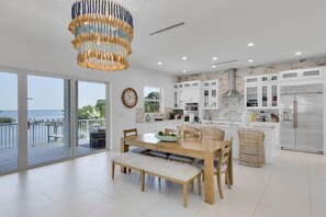 A modern kitchen with white cabinets, a stainless steel refrigerator, and a dining area with a wooden table and bench. - Gulfside Oasis a Dream on the Gulf (Marathon)