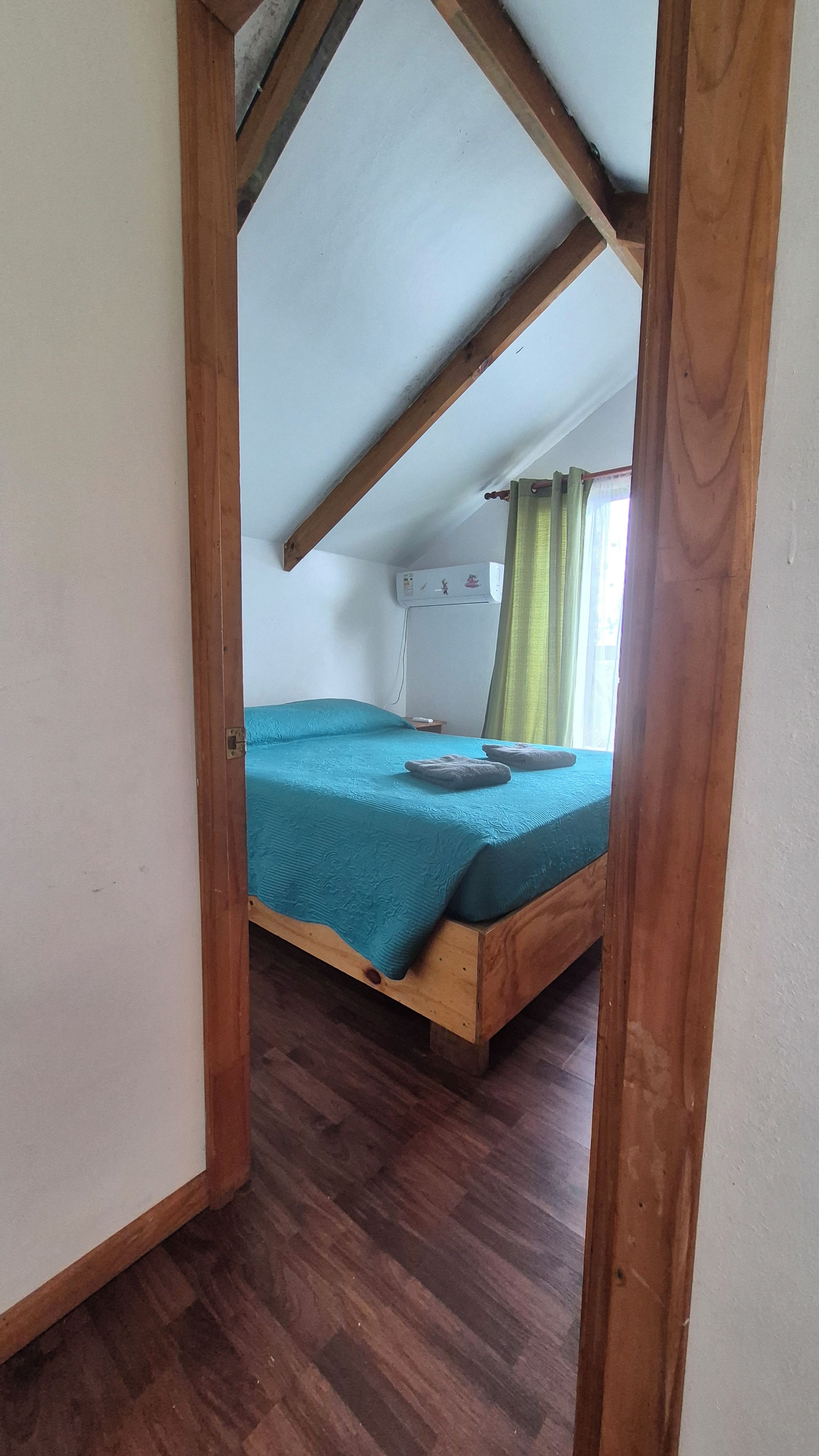 A room with a wooden bed, a small bedside table, and a window with curtains.