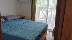 Un dormitorio con cama de madera, ventilador de techo, ventana con cortinas y vista al exterior.