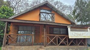 A two-story wooden cabin with a balcony, large windows, and a porch area.