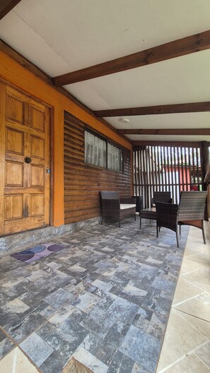 A covered outdoor area with a wooden door, wicker furniture, and a tiled floor.