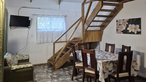 Un comedor con una escalera de madera, un televisor montado en la pared y una mesa con manteles florales.