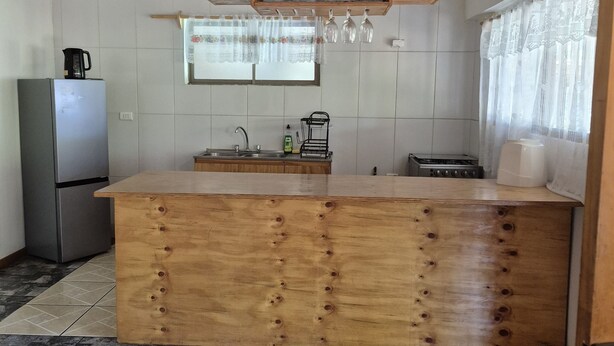 Una cocina con una isla de madera, un refrigerador y un ventanal con cortinas.