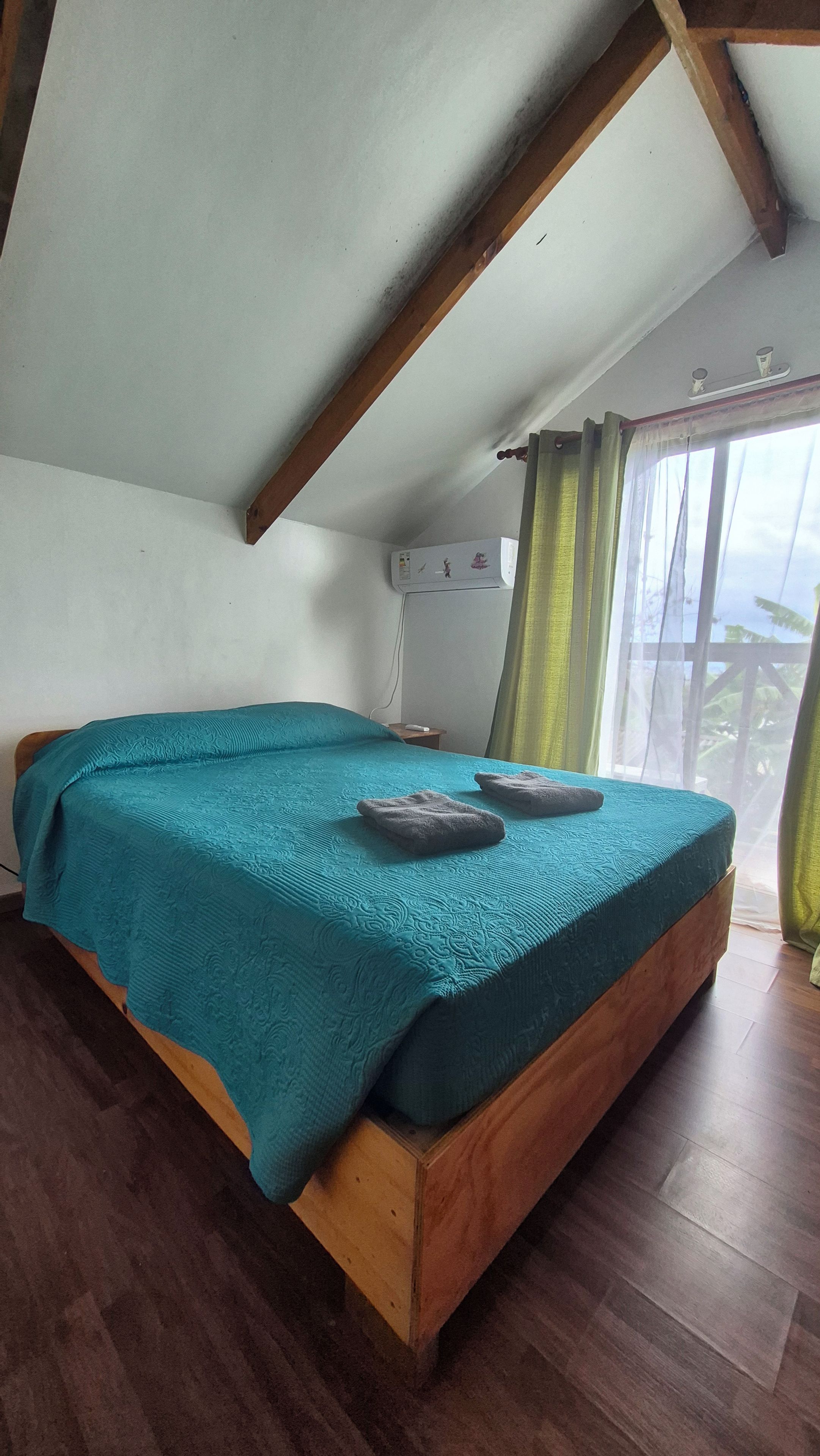 A bedroom with a wooden bed, a teal bedspread, and a window with curtains.