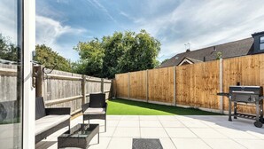 Eine Terrasse mit Grill, Gartenmöbeln und einem Holzzaun.
