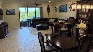 A spacious living area with a sectional sofa, a dining table with chairs, a fireplace, and a bookshelf. - Gated Tuscan Paradise: 4BR/3BA Home + Lagoon Pool, Tennis & Fitness Club Access (Venice)