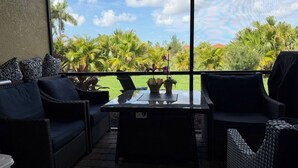 A balcony with wicker furniture, a glass table, and a view of palm trees and a clear sky. - Gated Tuscan Paradise: 4BR/3BA Home + Lagoon Pool, Tennis & Fitness Club Access (Venice)