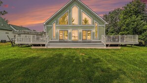 A two-story house with a large front porch, a covered porch area, and a well-maintained lawn. - Portage Lake Beachfront with Dock at North Point (Onekama)