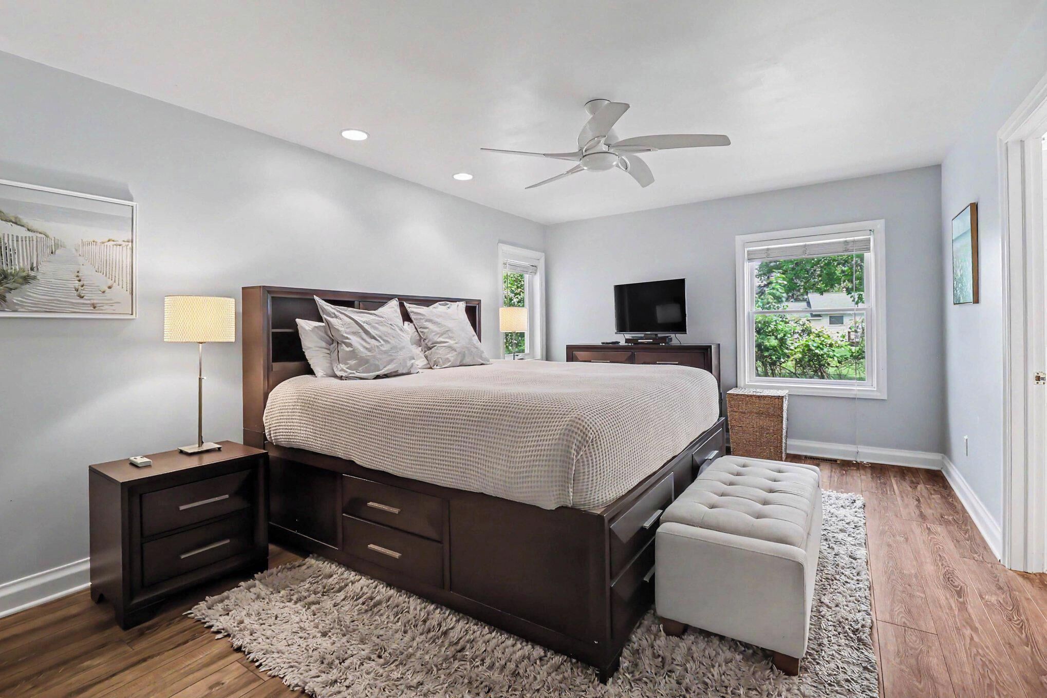 A bedroom with a bed, nightstands, a TV, a ceiling fan, and a window.