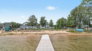 A waterfront property with a clear walkway leading to the water, surrounded by houses and trees. - Portage Lake Beachfront with Dock at North Point (Onekama)