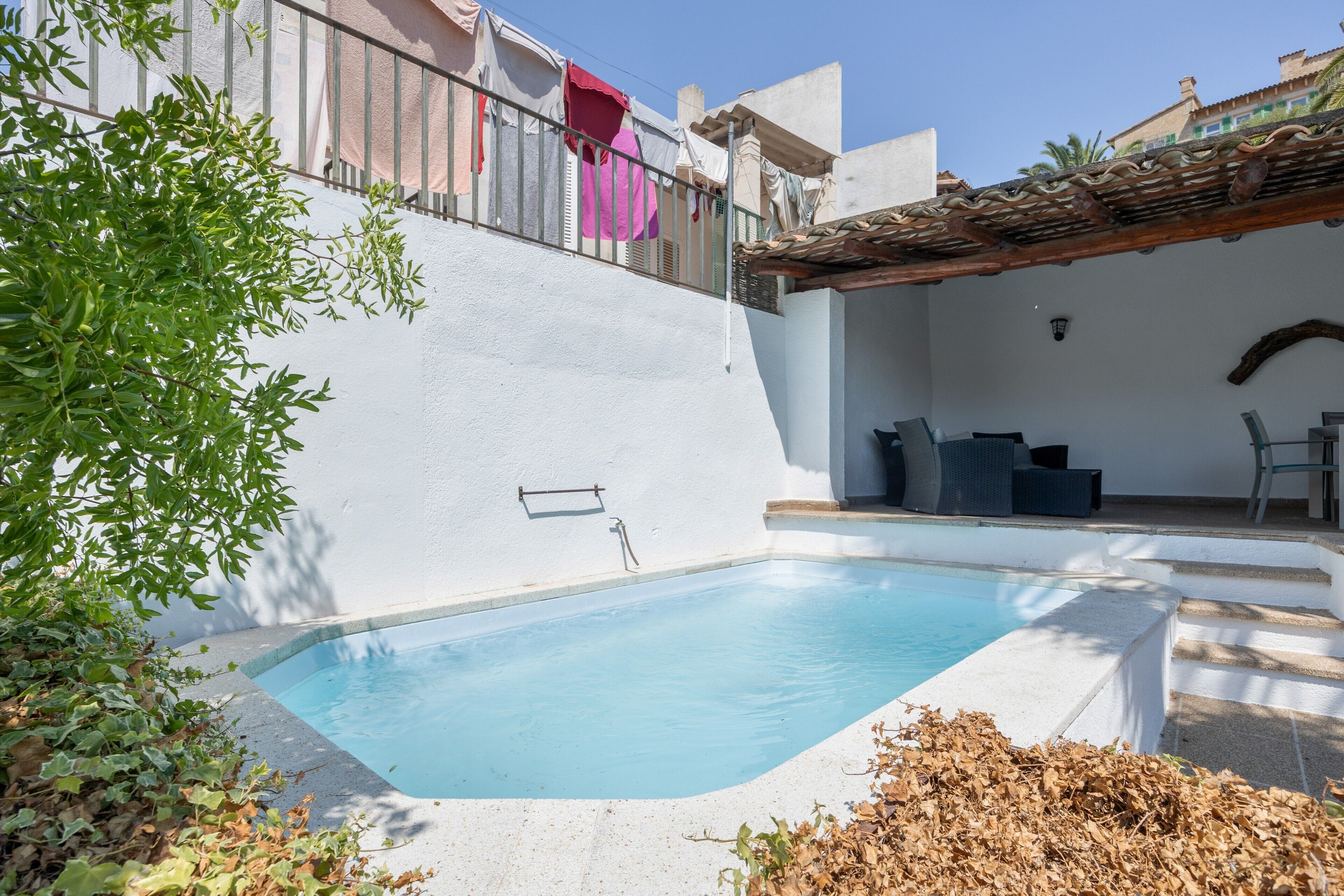 Uma piscina com parede branca, guarda-corpo de metal e pérgola.