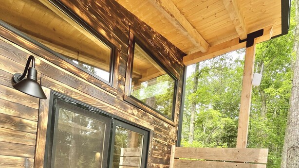 Una terraza de madera con una puerta de cristal, dos sillas Adirondack y un banco.