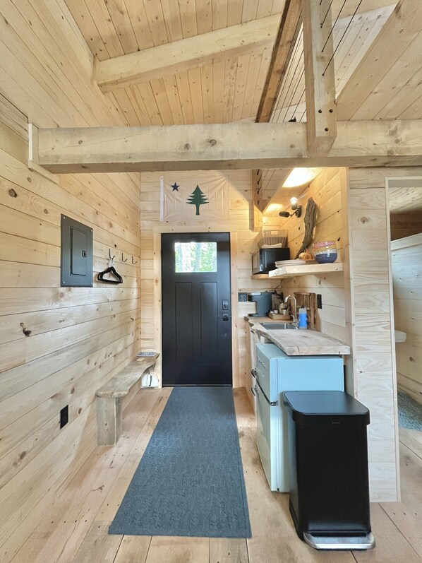 Un interior de madera con una puerta negra, una pequeña zona de cocina y un cubo de basura.