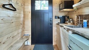 Interior de madera estrecho con una puerta negra, una ventana pequeña, un microondas, un lavamanos y un refrigerador.
