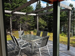 Una terraza de madera al aire libre con una mesa y sillas de vidrio, rodeada por un bosque.