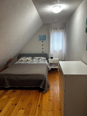 Un dormitorio con cama, mesita de noche, escritorio, ventana con cortinas y luz en el techo.