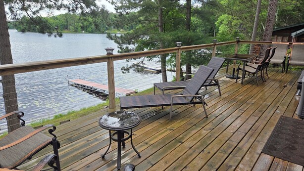 Une terrasse en bois avec des meubles d’extérieur, une petite table et une rambarde donnant sur un lac.