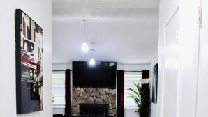 Een hal die uitkomt op een woonkamer met een stenen openhaard, een flatscreentelevisie en een groot schilderij aan de muur.