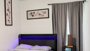 Een slaapkamer met een bed, een nachtkastje, een wandlamp en twee florale foto's in lijsten.