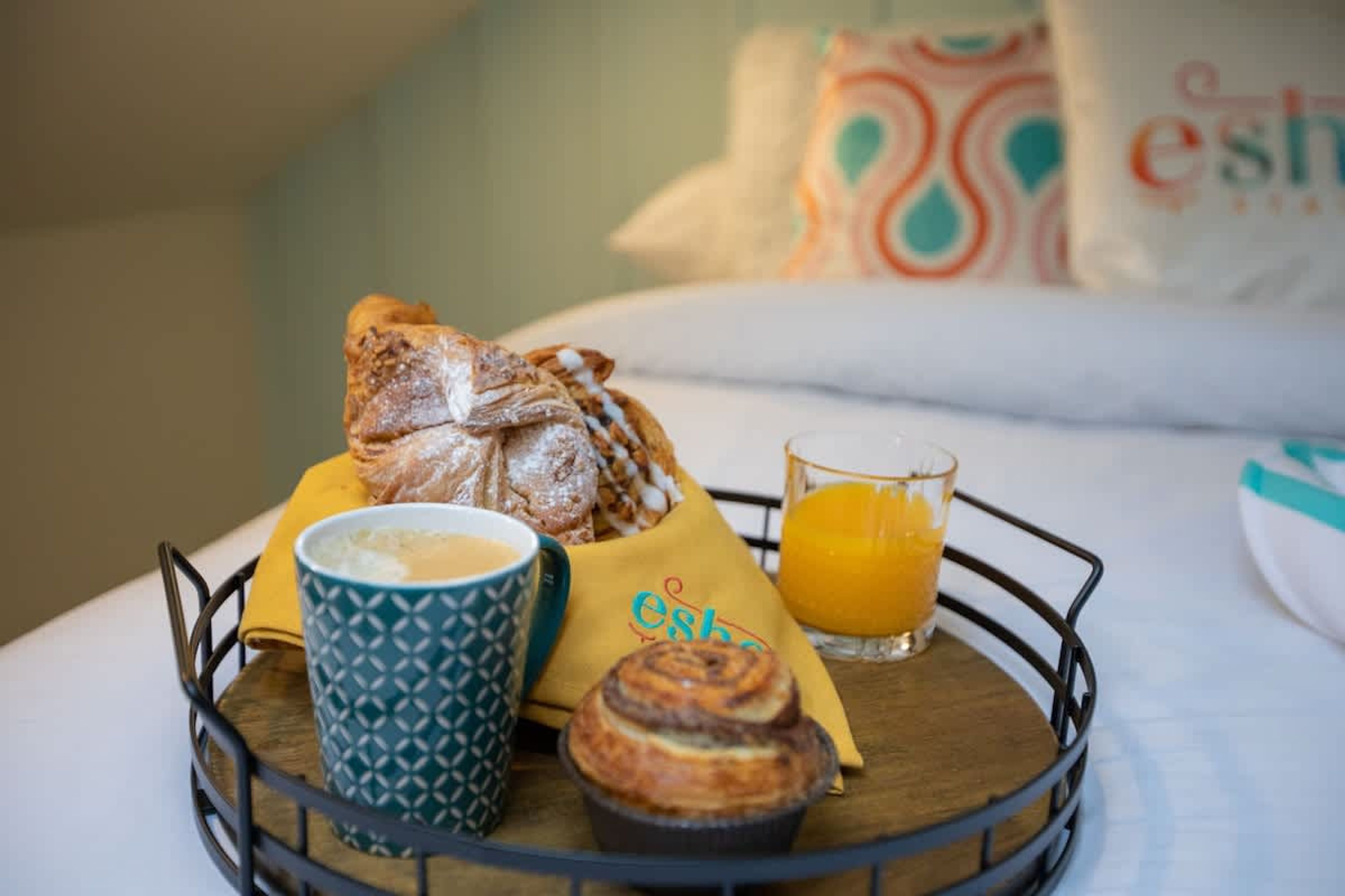 A breakfast tray with pastries, a muffin, a cup of coffee, and a glass of orange juice on a bed.