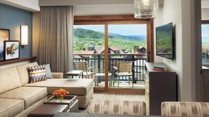 Una camera d'albergo con balcone, un divano, un tavolino da caffè e una televisione.