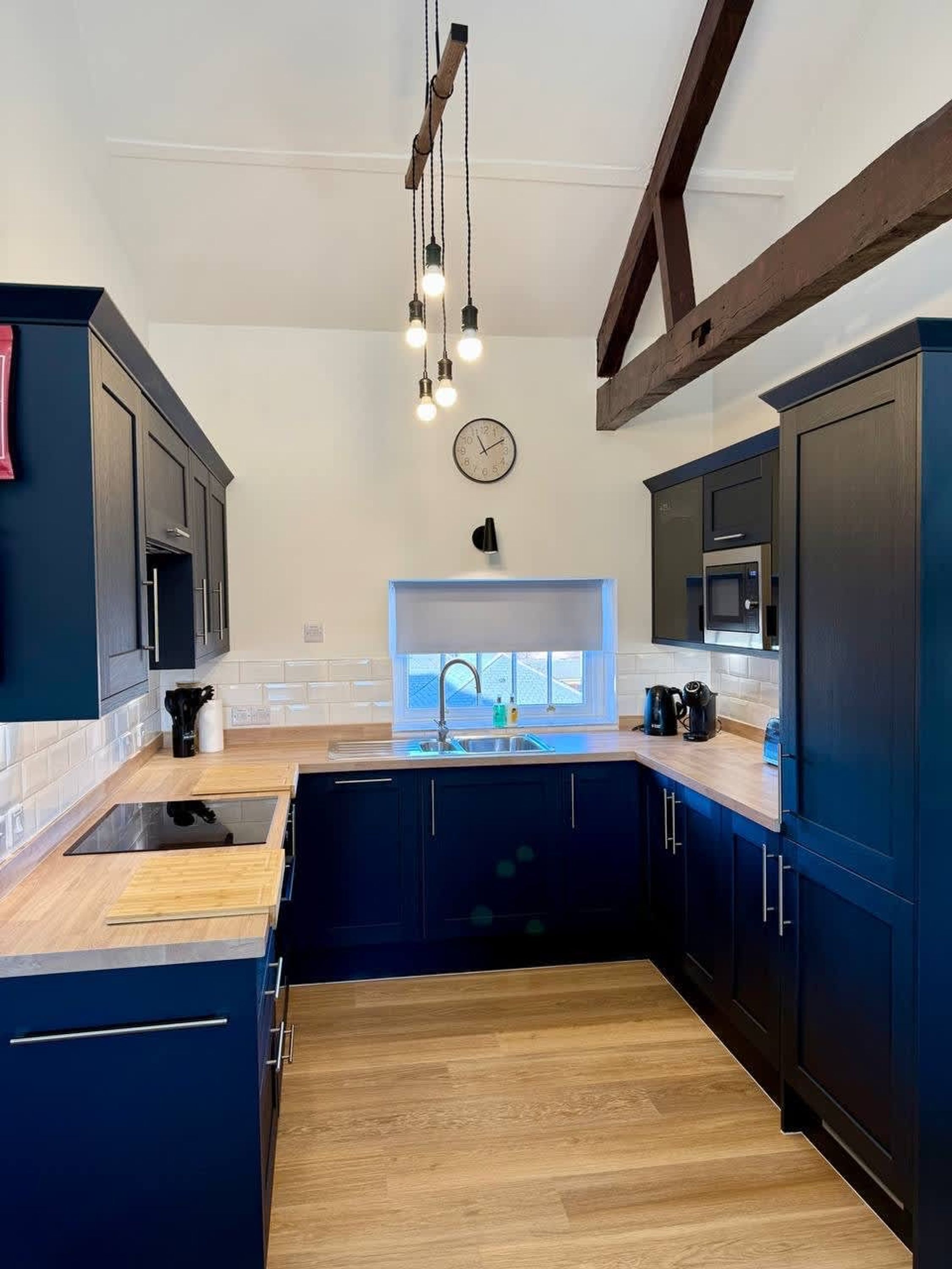A modern kitchen with dark cabinetry, a wooden countertop, a built-in stove, and pendant lighting.