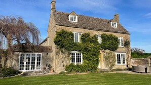 A stone house with a large lawn, a barbecue area, and a view of the countryside. - Stunning Countryside House with Pool and Hot Tub (Wiltshire)