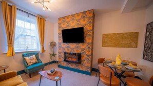 Una sala de estar con chimenea, una mesa de comedor con sillas, un sofá y un televisor montado en la pared.
