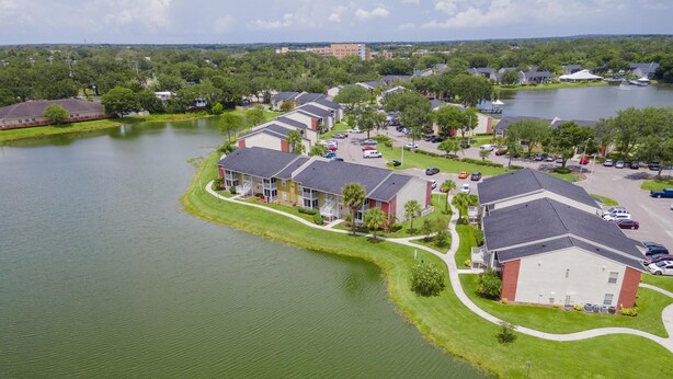 A residential area with houses along a lake, featuring a large building with a red roof and a smaller building with a white facade. - Lake Front - Corner Unit - 2 Bedroom 2 Bath (Brandon)
