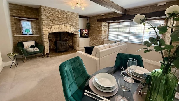 A dining area with a stone fireplace, green upholstered chairs, a round table set for four, and a large green vase. - Ground floor apartment in 18th century building (Gloucestershire)