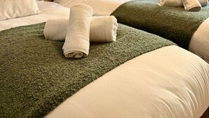 A hotel room with two beds, each with a green blanket and white pillows, and a headboard. There is a window with blinds and a plant on the windowsill. - Ground floor apartment in 18th century building (Gloucestershire)