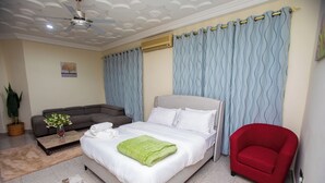 Una camera da letto con un letto, una poltrona rossa, un divano grigio, una ventola a soffitto e un condizionatore d'aria a parete.