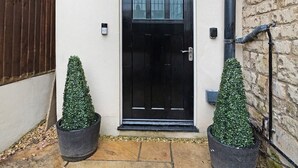 A black door with a small step leading up to it, flanked by two potted topiaries, a stone-paved entrance, and a brick wall. - 4BD 3Bath 2Car Drive Garden Games room Nr Hospital (Gloucestershire)