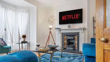 A living room with a fireplace, a television displaying 'NETFLIX,' a blue sofa, and a coffee table.