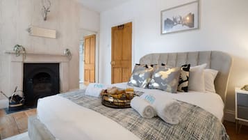 A bedroom with a fireplace, a bed with a grey headboard, and a basket of bread.