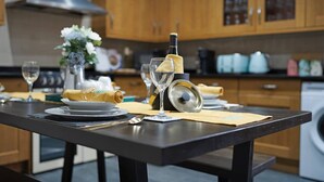 A kitchen with wooden cabinets, a stainless steel range hood, a dining table with a bottle, glasses, and a napkin. - 4BD 3Bath 2Car Drive Garden Games room Nr Hospital (Gloucestershire)