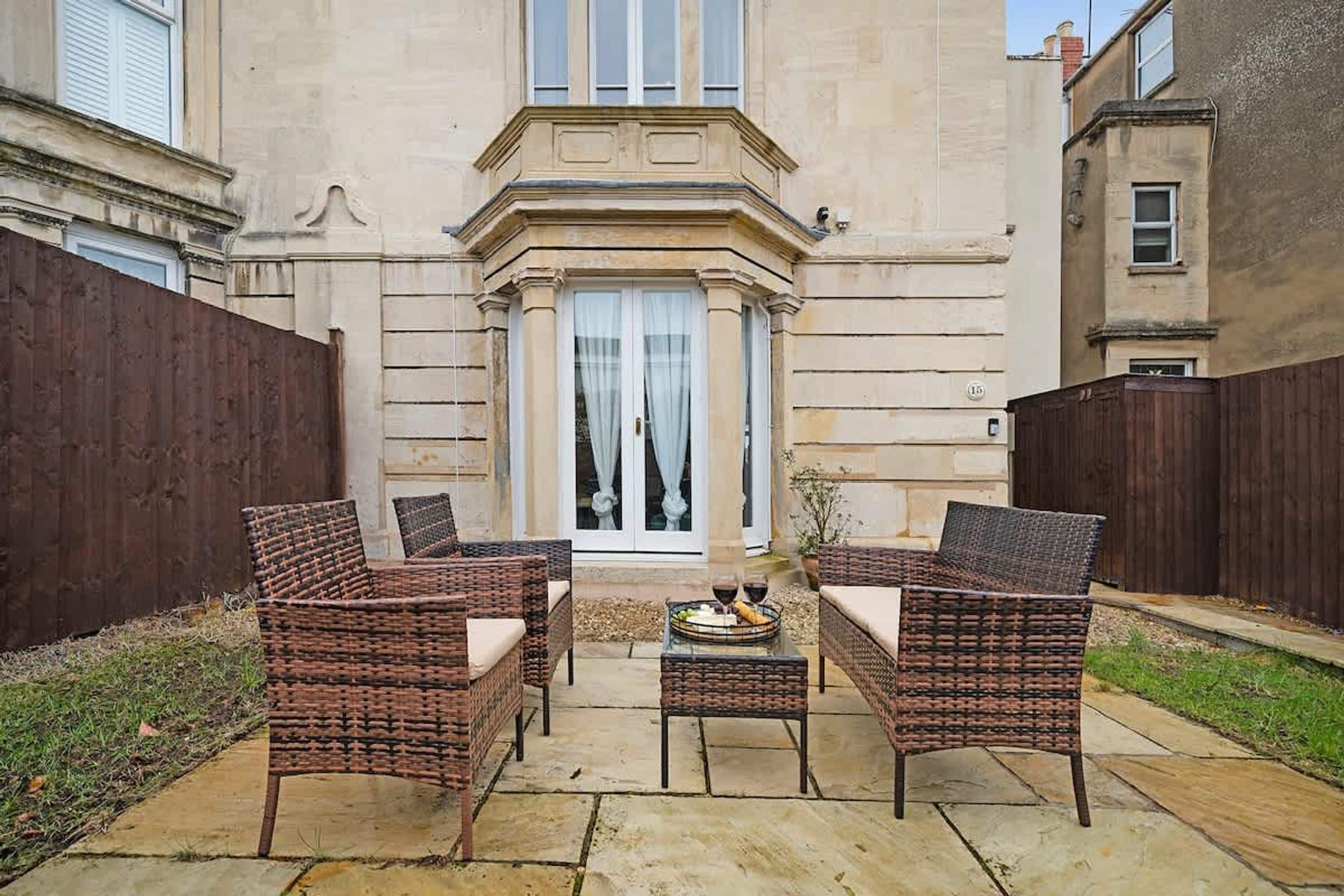 A patio with wicker furniture, a table with a wine bottle, and a building with a stone facade.