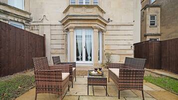 A patio with wicker furniture, a table with a wine bottle, and a building with a stone facade.