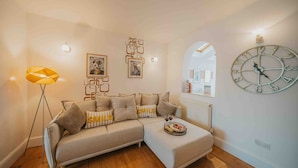 A living room with a sofa, a floor lamp, wall art, a clock, and a radiator. - Cotswolds   2BD   1 Bath   Garden   City Centre (Gloucestershire)